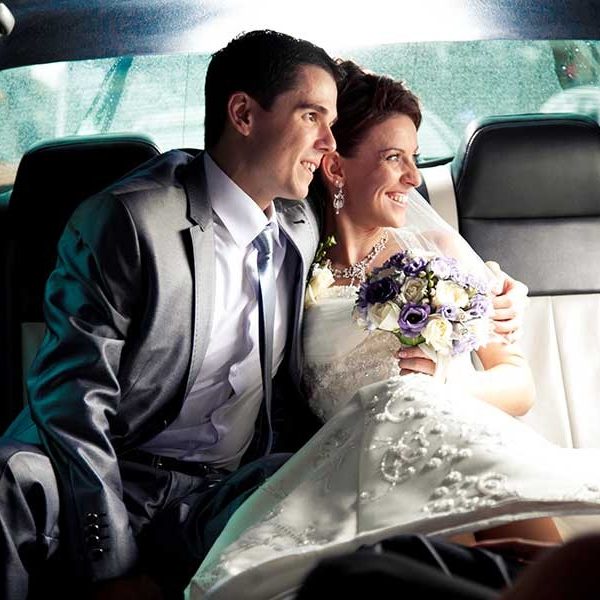 Bridal couple smiling together in a limo car, holding a bouquet and dressed in wedding attire.