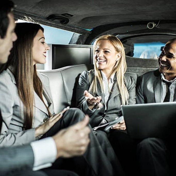 Four professionals in suits engaged in conversation inside a limousine.
